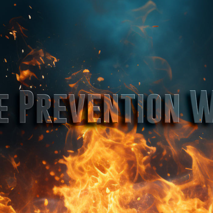 The image depicts the words “Fire Prevention Week” in bold capital letters, set against a backdrop of swirling smoke and rising flames. The text is front and center, with intense orange flames consuming the bottom half of the frame, while dark smoke cloud